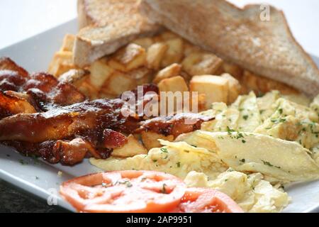 des tranches de bacon de porc croustillantes et bien cuites frites ou grillées avec des hash browns et des toasts avec des tomates sur plaque dans une vue rapprochée pour le déjeuner ou le dîner du petit déjeuner Banque D'Images