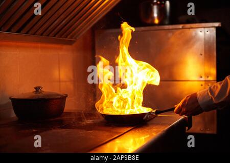 Flambe. Feu dans la poêle à frire. Chef professionnel dans une cuisine commerciale. Faites frire des aliments dans une poêle moulante sur la table de cuisson dans la cuisine extérieure Banque D'Images