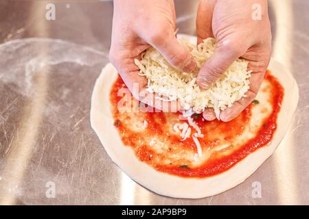 Cuisson de la pizza. Organise les ingrédients du fromage sur la préforme de pâte. Gros plan de la main du boulanger du chef dans un tablier blanc uniforme cuisinier à la cuisine Banque D'Images