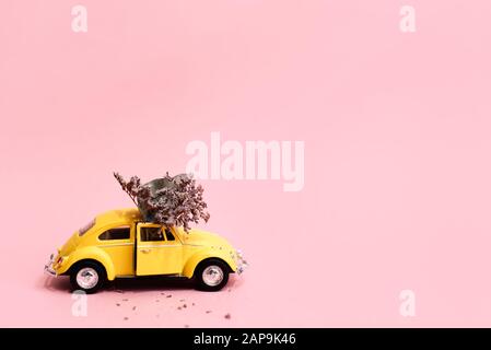 Azov, Russie 8 - Jan 2020. Voiture jaune rétro jouet livrant bouquet de fleurs boîte sur fond rose. Carte du 14 février, Saint Valentin. Fleurs deliv Banque D'Images