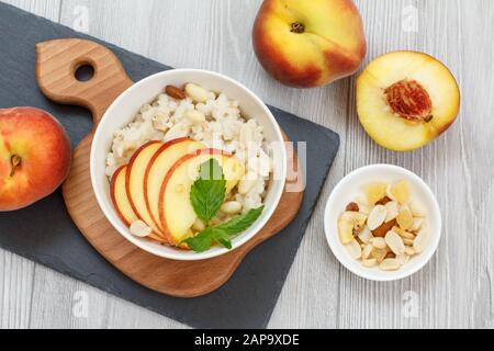 Porridge de sorgho avec morceaux de pêche, noix de cajou et amandes dans des bols en porcelaine, pêches fraîches sur bois et panneaux de pierre. Sorgho végétalien sans gluten Banque D'Images