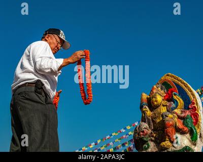 Homme local offrant une terre de fleurs à une image d'une aubaine à Boudha Stupa Banque D'Images