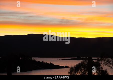 Des oranges lumineuses coucher de soleil au bord du lac Jindabyne dans les montagnes enneigées australie Banque D'Images