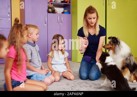 Petit groupe d'enfants jouant avec le chien de thérapie dans la maternelle Banque D'Images