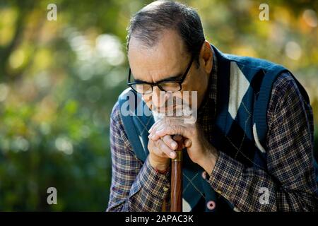 Un vieil homme attentif assis seul sur le parc Banque D'Images