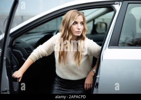 Belle femme blonde dans la jupe en cuir sortir de la voiture Banque D'Images