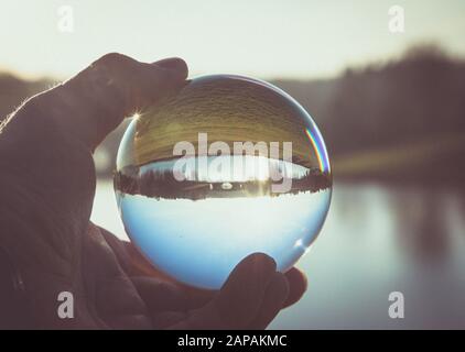 Une main tenant une balle de lensball encapsule une image rendue d'un pont sur un lac pendant un après-midi hivers. Banque D'Images