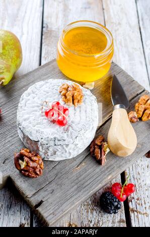Différents types de Délicieux fromages sur une planche en bois et de nombreux en-cas, noix, miel, baies, olives sur une vieille table en bois blanc. Ingrédients alimentaires de retour Banque D'Images