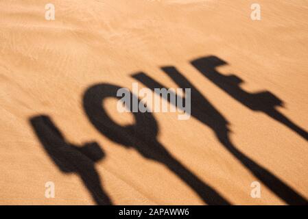 gros plan de l'ombre de deux personnes tenant quelques lettres formant le mot amour sur leurs têtes sur le sable d'une plage Banque D'Images