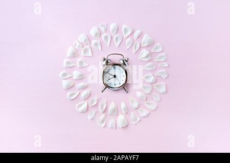 Réveil et pétales délicats de roses blanches sur fond rose. Cadre de fleur. Le concept de minimalisme. Plat, vue du dessus. Banque D'Images