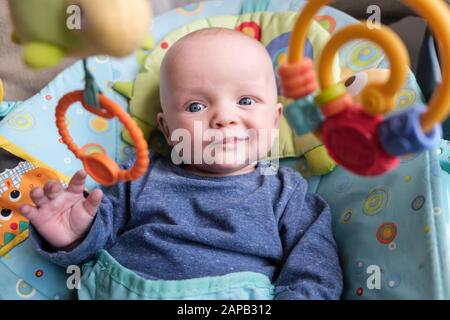 Style de vie quotidien authentique d'un bébé garçon de cinq mois avec une expression puzzicale dans une chaise d'activité regardant des jouets suspendus Grande-Bretagne Banque D'Images