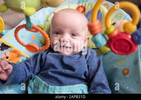 Image authentique d'un jeune garçon de cinq mois heureux dans une chaise d'activité souriant et regardant des jouets suspendus. Angleterre, Royaume-Uni, Grande-Bretagne Banque D'Images