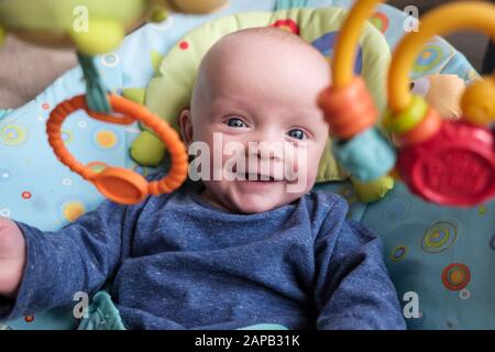 Un jeune garçon heureux de cinq mois dans une chaise d'activité souriant et regardant vers l'avant des jouets suspendus. Angleterre, Royaume-Uni, Grande-Bretagne Banque D'Images