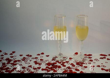 Deux verres à champagne remplis de vin entouré de confettis en forme de coeur sur un fond blanc avec espace de copie. Banque D'Images