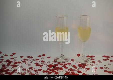 Deux verres à champagne remplis de vin entouré de confettis en forme de coeur sur un fond blanc avec espace de copie. Banque D'Images