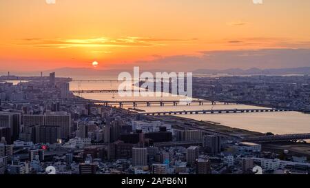 Vue aérienne au coucher du soleil sur la ville d'Osaka avec la rivière, le soleil rond et le ciel doré, vue depuis l'Umeda Sky Building. Banque D'Images