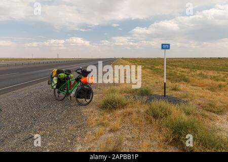Vélo pour un voyageur se tient sur la route près d'un kilomètre panneau, Kazakhstan Banque D'Images