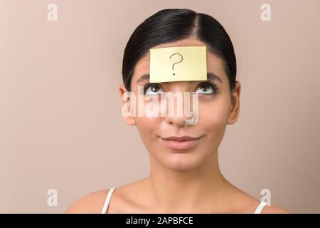 jeune femme avec un autocollant sur son front avec un point d'interrogation dessus sur un fond propre Banque D'Images
