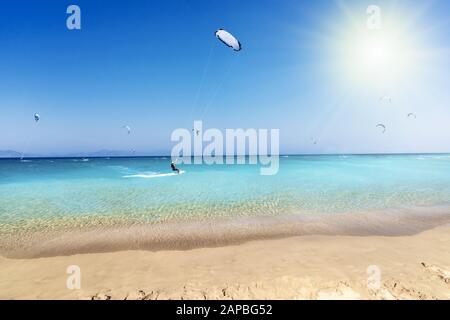 Les surfeurs du cerf-volant se rendent sur les vagues de la plage en mer Égée, dans le ciel bleu et dans les rayons du soleil (Rhodes, Grèce) Banque D'Images