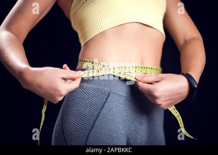 Femme avec des cheveux blond courts dans des vêtements de sport measusing sa taille. Forme physique, régime alimentaire et concept de santé Banque D'Images