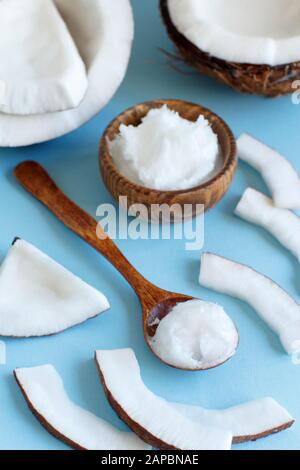 Huile de coco dans un bol en bois avec une cuillère près sur un fond bleu clair Banque D'Images
