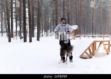 un jeune homme joue avec un chien dans un parc de chiens dans une forêt hivernale pendant une chute de neige Banque D'Images