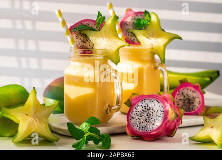 Un gros plan de deux smoothies aux fruits exotiques tropicaux à côté d'une fenêtre ensoleillée, prêts à boire. Banque D'Images