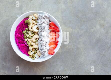 Bol de smoothie pour petit déjeuner sain avec pitaya, noix de cajou, flocons de noix de coco et fraise sur fond gris. Espace de copie. Banque D'Images