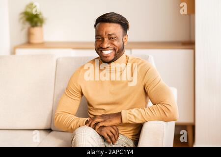 Joyeux Homme Africain Américain Smiling Assis Sur Canapé À La Maison Banque D'Images