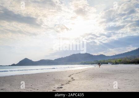 Amérique Centrale, Nicaragua, San Juan Del Sur. Une femme surfant laissant des pieds sur une plage de sable blanc vide au coucher du soleil Banque D'Images