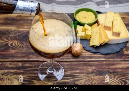 Verser de la bière rouge abbatiale belge en verre et en pierre avec des fromages faits par des moines de lait de vache avec fenugrec et graines de moutarde près Banque D'Images