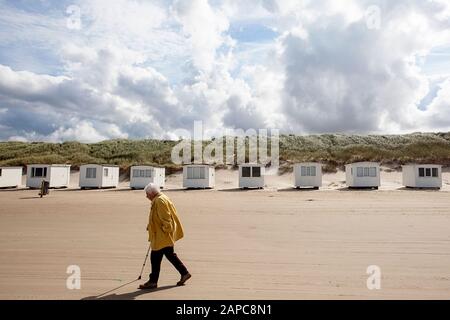 Personne senior avec un bâton marchant par la ligne de cabines de vacances de baignade sur la plage de Løkken, Danemark Banque D'Images