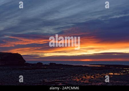 Aube à la plage Rocky North d'Arbroath avec la lumière rouge et orange reflétant dans les Piscines de Rock quand le soleil se lève à l'horizon. Banque D'Images