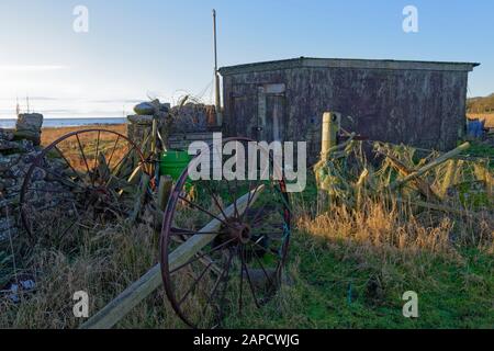 Une paire de vieilles roues de chariot en métal rouillé vues garées derrière un mur de pierre à côté d'une petite hutte de ferme en réparation dans un champ à l'extérieur du sentier côtier. Banque D'Images