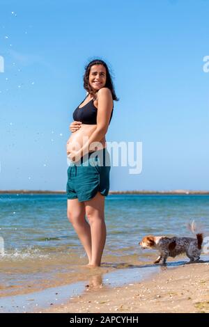 Femme enceinte qui s'amuse avec de l'eau sur la plage. Banque D'Images