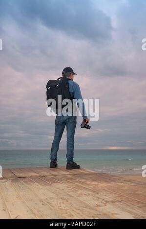 Vue arrière d'un photographe transportant un appareil photo donnant sur l'océan Banque D'Images