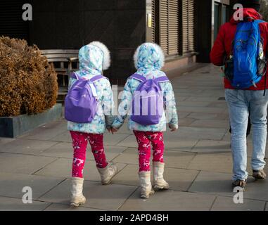 Deux petites sœurs jumelles en vêtements d'hiver assortis qui s'éloignent dans les rues de Londres, au Royaume-Uni Banque D'Images