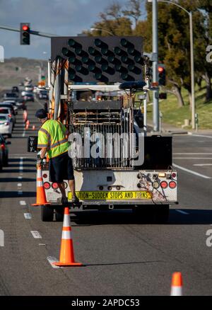 Travailleur derrière un camion utilitaire plaçant des cônes de circulation orange vif sur la chaussée pour le contrôle de la circulation sur une scène d'accident Banque D'Images