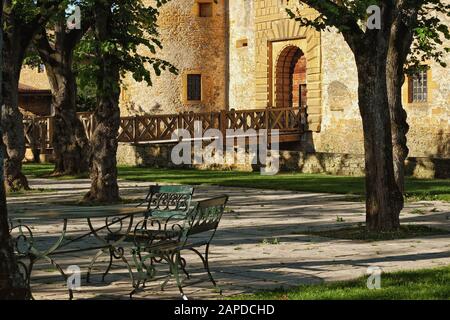 Les murs en pierre dorée du Château de Bagnols sous le soleil d'été de la terrasse pavée du jardin, arbres fruitiers et meubles de jardin en fer forgé Banque D'Images