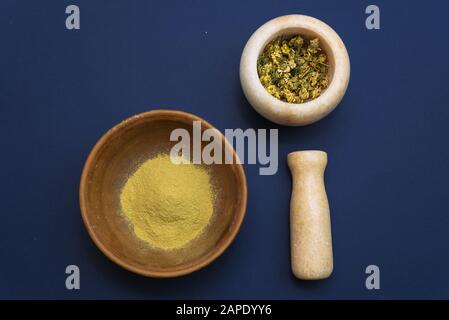 Mortier de marbre avec camomille séchée pour cosmétiques naturels. Bols en argile et en verre avec poudre jaune ou argile et fleurs. Plat, bleu classique. Banque D'Images