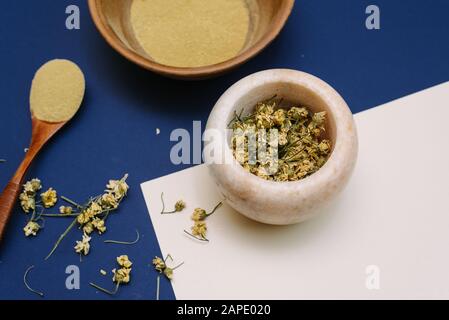 Mortier de marbre avec camomille séchée pour cosmétiques naturels. Bols en argile et en verre avec poudre jaune ou argile et fleurs. Plat, bleu classique. Banque D'Images