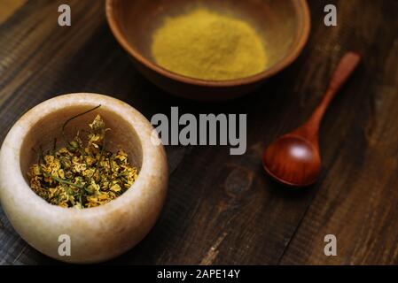 Mortier de marbre avec camomille séchée pour cosmétiques naturels. Bol en argile avec poudre jaune ou argile et fleurs sur fond en bois. Pose plate. Banque D'Images