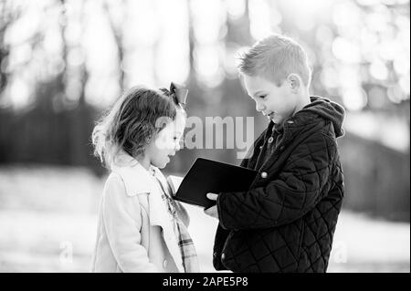 Échelle de gris de deux enfants lisant la bible dans un jardin couvert par la neige sous la lumière du soleil Banque D'Images