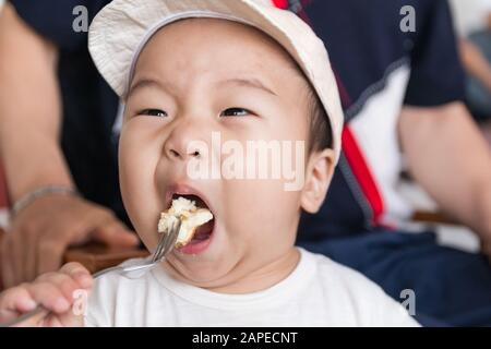 Petit garçon asiatique mangeant du pain au café Banque D'Images