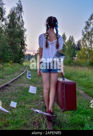 Une adolescente promenades le long des voies de chemin de fer avec une vieille valise et jette les vieilles photos. Banque D'Images