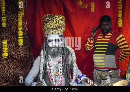 Un homme parle à son mobile à côté d'une Naga Sadhu dans un camp transiste de Ganga Sagar à Kolkata, en Inde. Banque D'Images