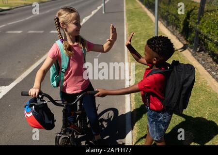 Les écoliers debout sur le pavé, tenant un vélo et haut fiving Banque D'Images