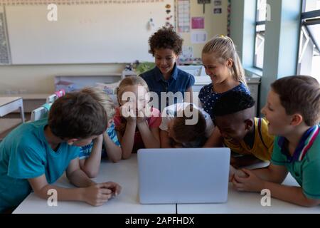 Groupe d'écoliers utilisant un ordinateur portable dans une salle de classe de l'école primaire Banque D'Images