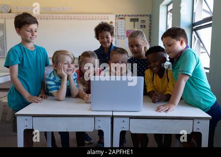 Groupe d'écoliers utilisant un ordinateur portable dans une salle de classe de l'école primaire Banque D'Images