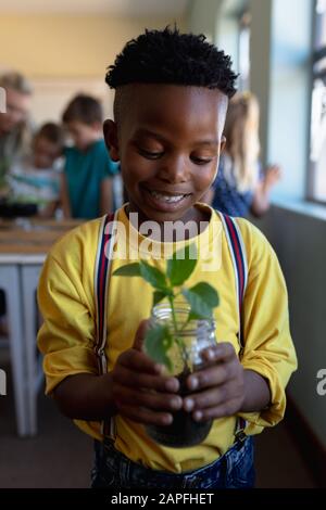 Un écolier tenant une plante de plantules dans un bocal de terre dans une salle de classe de l'école primaire Banque D'Images